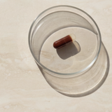 Brown capsule floating in a glass of water on a light surface