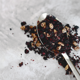 Spoonful of black and white speckled salt on a textured surface