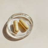 Two capsules in a clear glass dish on a light beige background