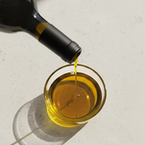 Olive oil being poured from a bottle into a glass bowl on a light background
