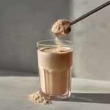 Spoon pouring powder into a glass of coffee on a neutral background