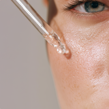 Close-up of a dropper applying clear liquid to skin near an eye.
