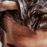 Close-up of a person washing their hair with shampoo, showing the texture and movement of the water and shampoo.