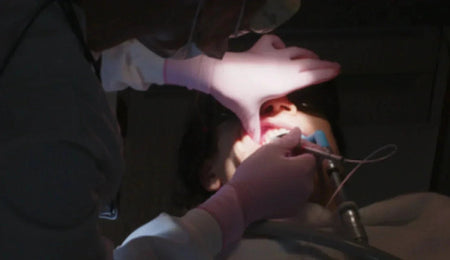 Dentist examining a patient's teeth with a dental tool under bright light.