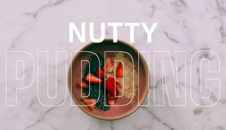 Bowl of nutty pudding topped with strawberries on a marble surface, with the words 'Nutty Pudding' overlaid in white text.