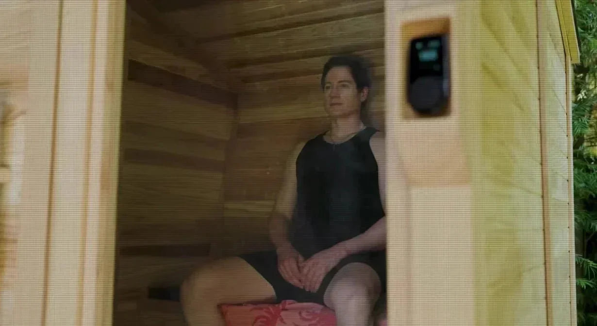 Bryan Johnson sitting inside a sauna with a digital temperature display visible on the wall.