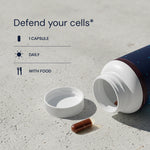 Open supplement bottle with a capsule on a concrete surface, text 'Defend your cells' displayed.