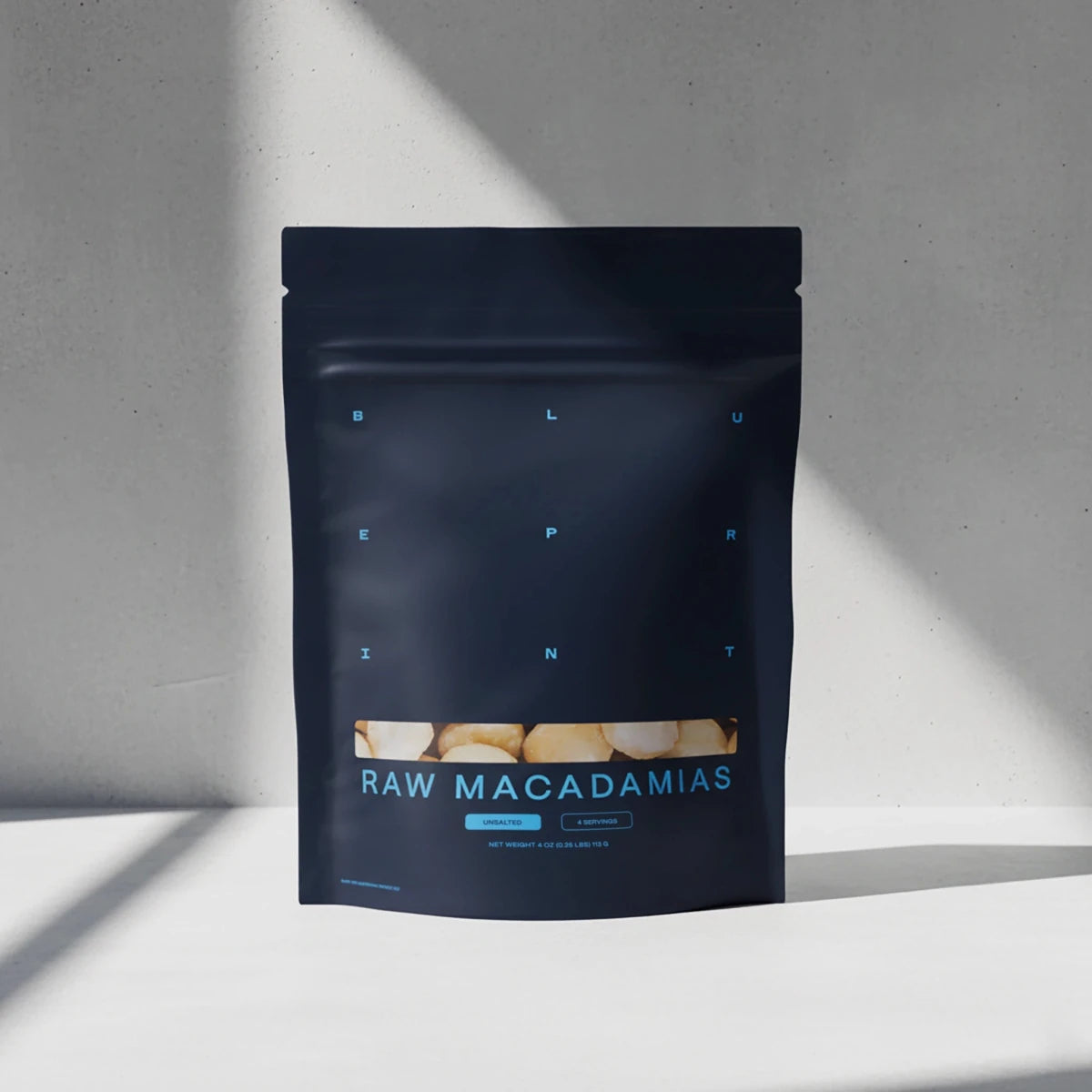 Dark blue package of raw macadamias on a light gray background