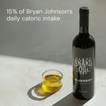 Bottle of 'Snake Oil Blueprint' with a glass of oil on a light surface.