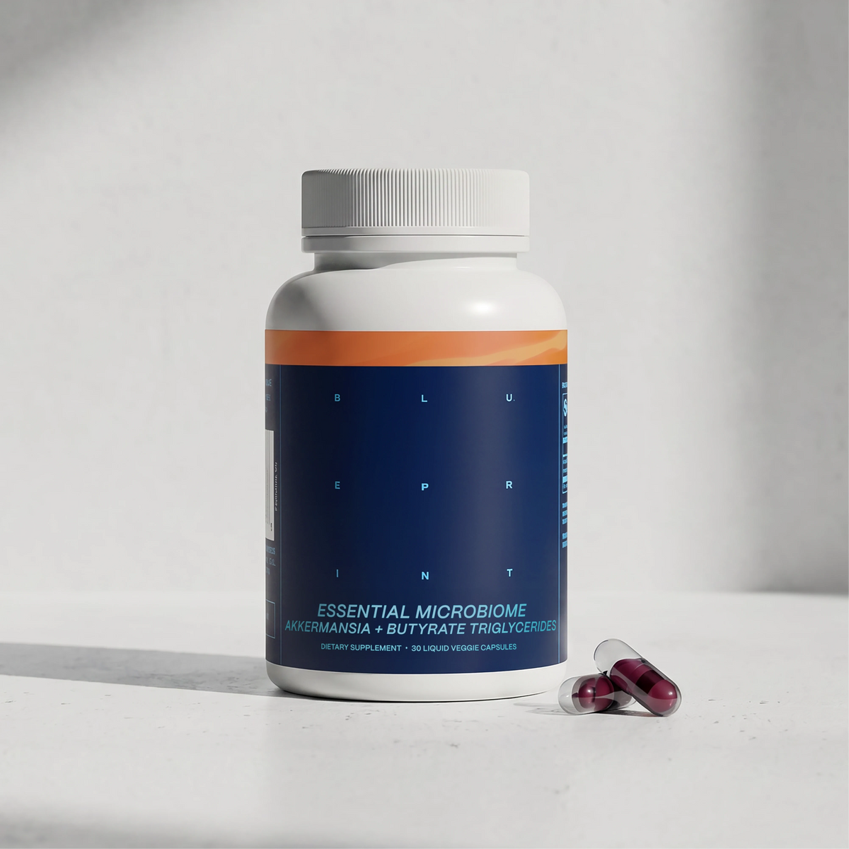 Blueprint Essential Microbiome supplement bottle with two magenta capsules on a white surface — longevity gut health