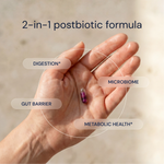 Hand holding a single Essential Microbiome postbiotic capsule with benefit labels — Blueprint longevity supplement