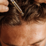 Person applying a dropper of oil to their hairline