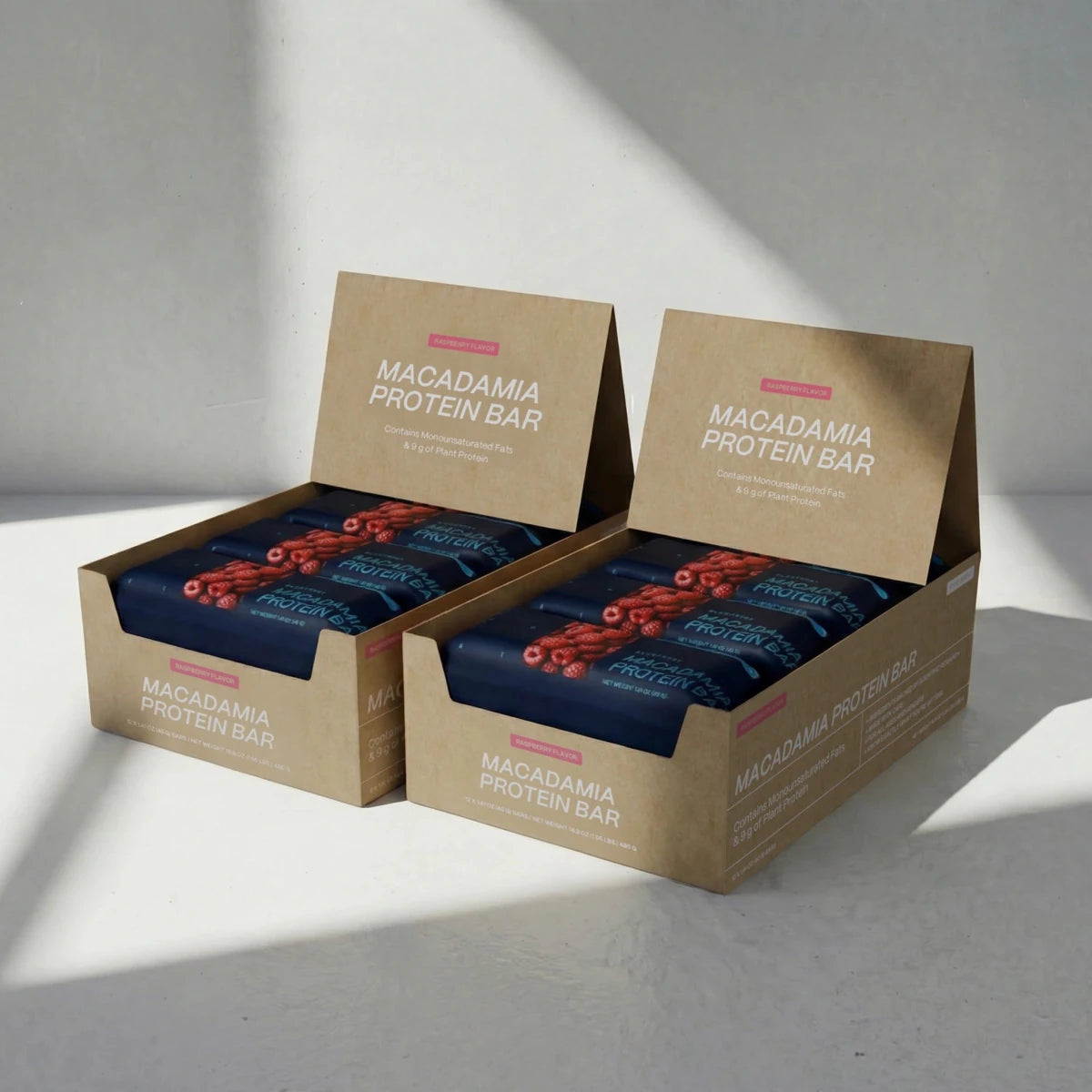Two boxes of Raspberry Macadamia Protein Bars on a light gray background