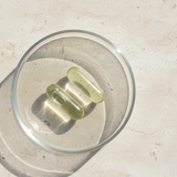 Two green capsules in a clear glass bowl on a beige surface