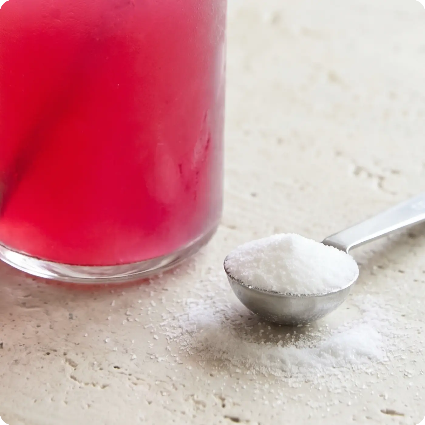 Red liquid in a glass with a spoonful of white powder on a light surface