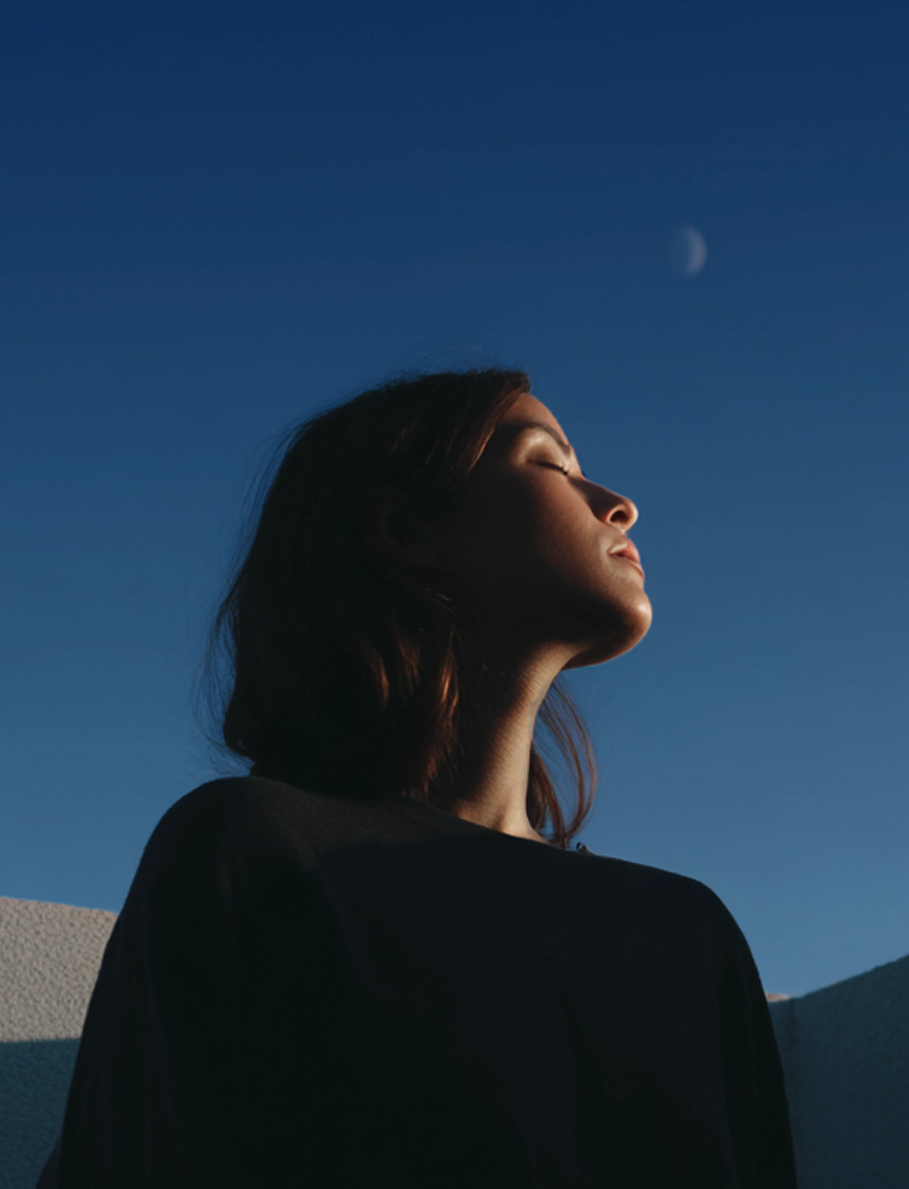 Person looking up at the moon against a clear blue sky