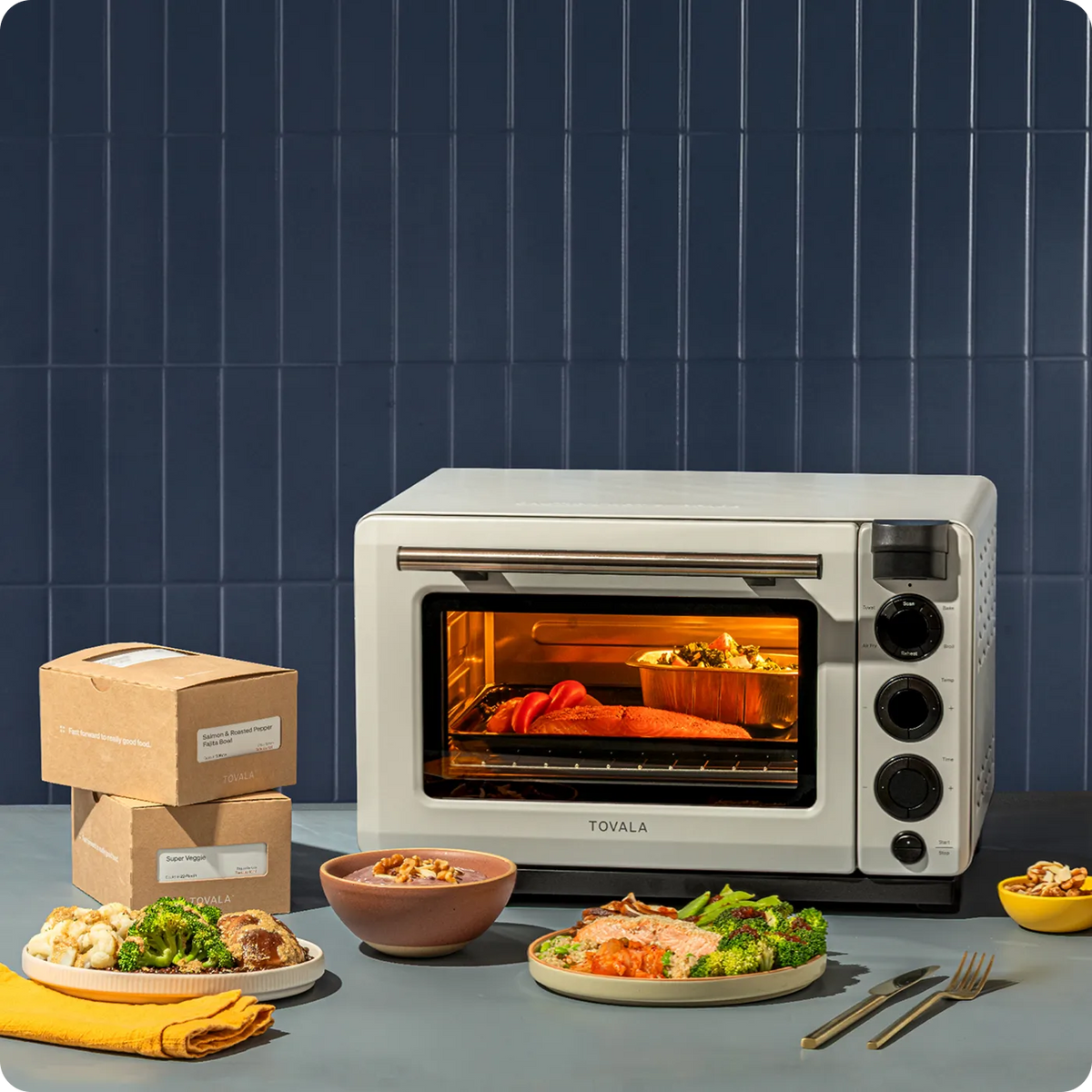 Tovala countertop convection oven in off-white on a kitchen counter with plated meals and shipping boxes
